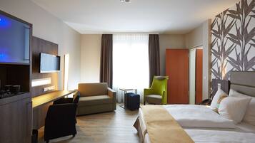 A hotel room with a bed, a desk, a television, a chair, and a sofa.