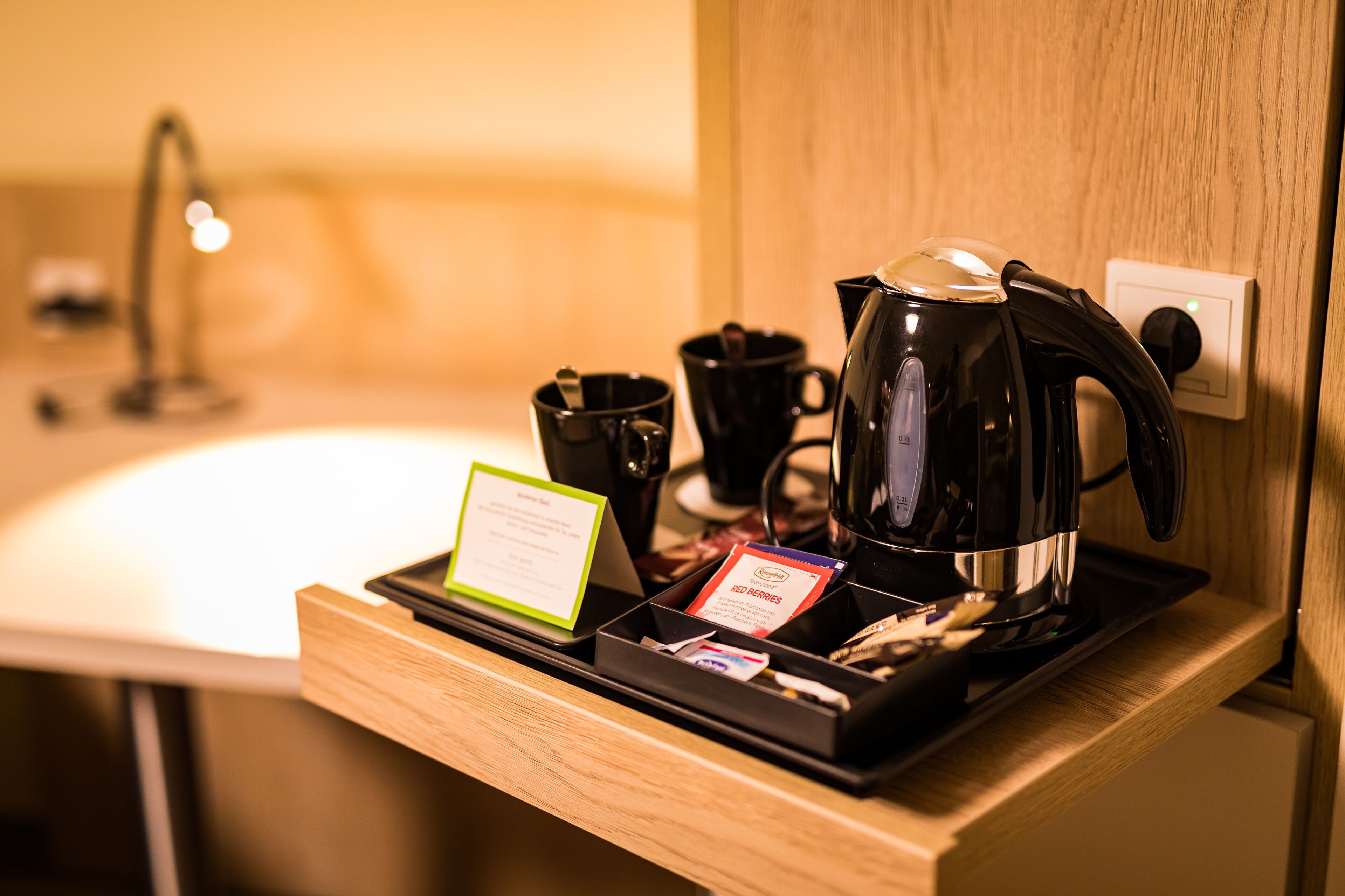 Eine Kaffeestation mit Wasserkocher, Tassen und einer Tablett mit einer Karte und einer kleinen Schachtel.