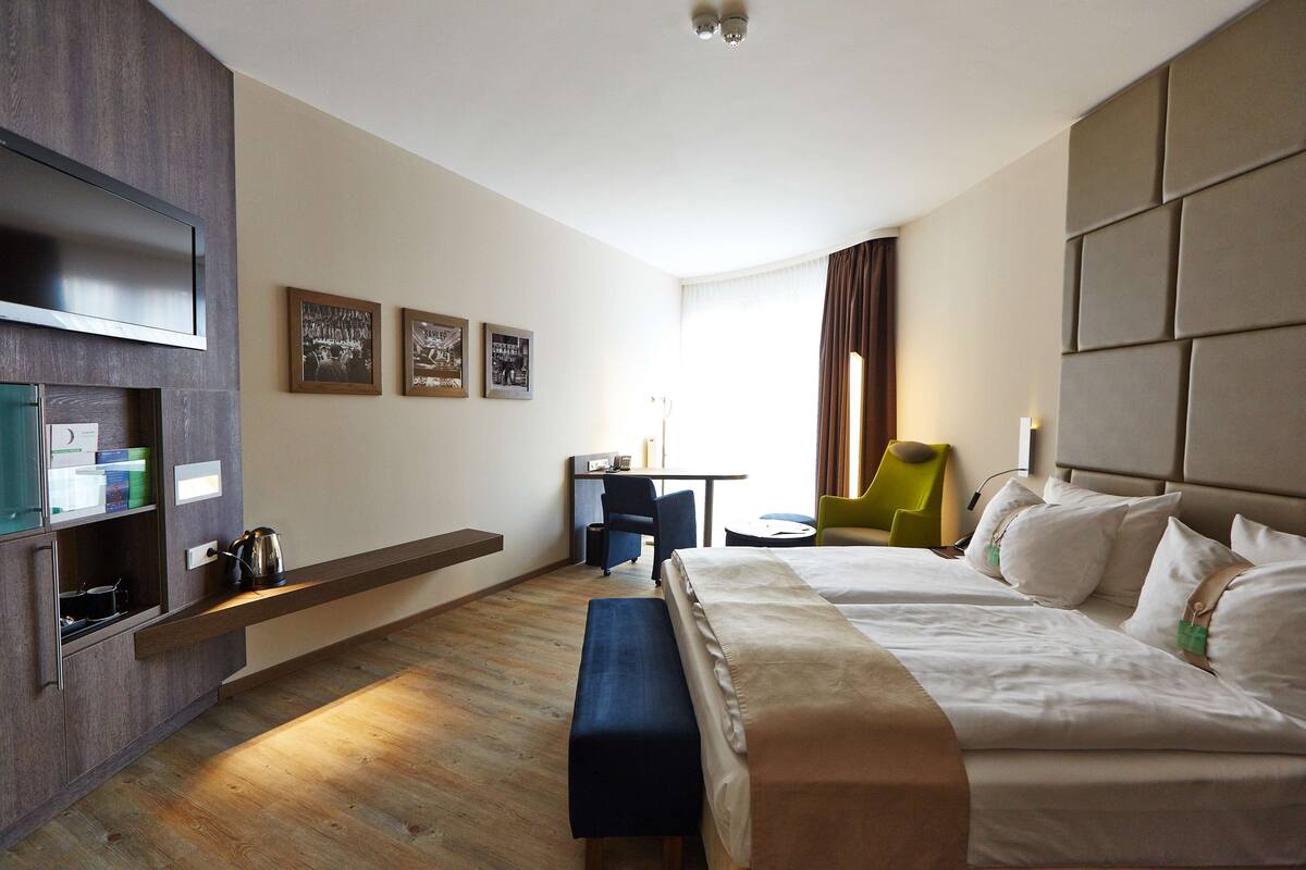 Habitación de hotel con cama, escritorio, silla, televisión y obras de arte en la pared.
