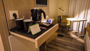 Habitación de hotel con estación de café, una mesita, una silla y un televisor montado en la pared.