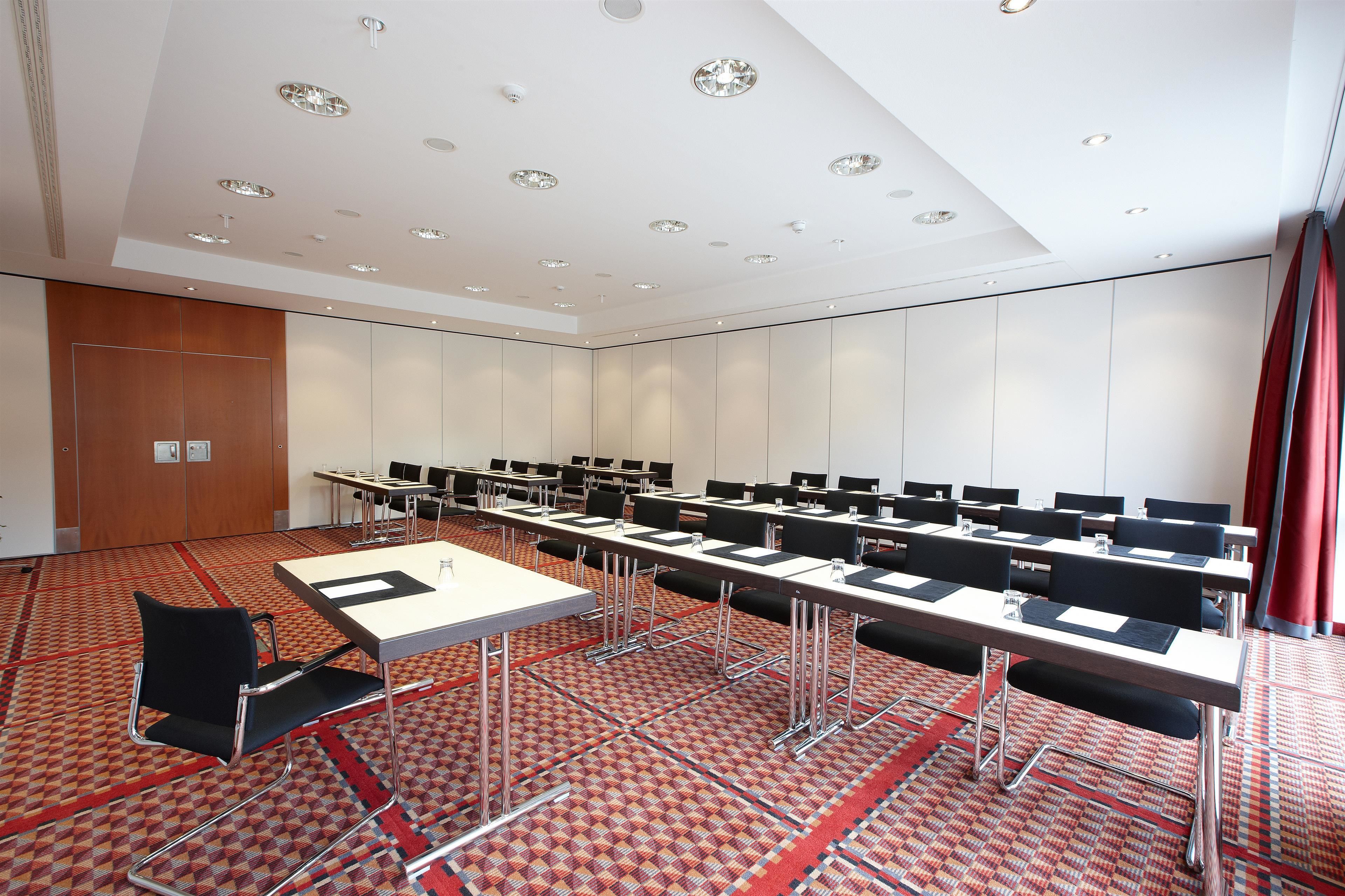 A conference room with multiple tables and chairs, a patterned carpet, and a ceiling with recessed lighting.