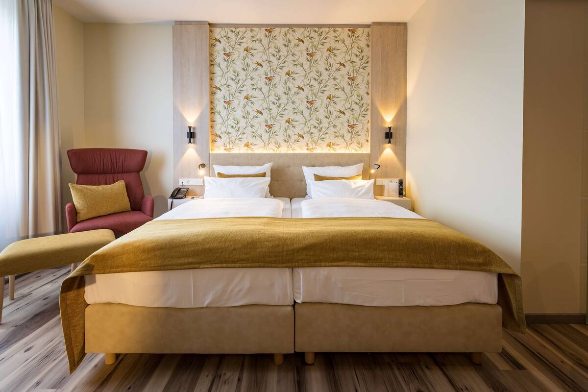 Una cama grande con cabecera, un sillón rojo, una mesita y una pared con diseño.