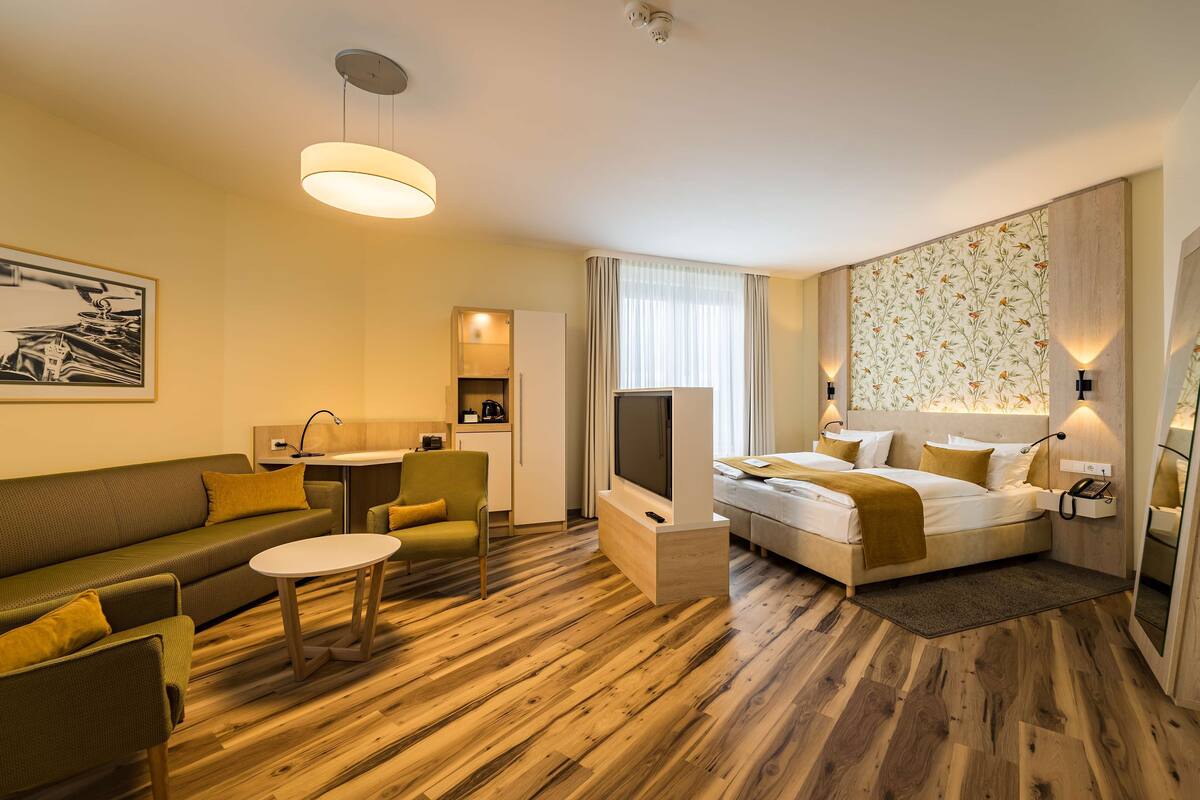 Una habitación de hotel moderna con sofá, una mesita, cama, televisor y área de cocina.