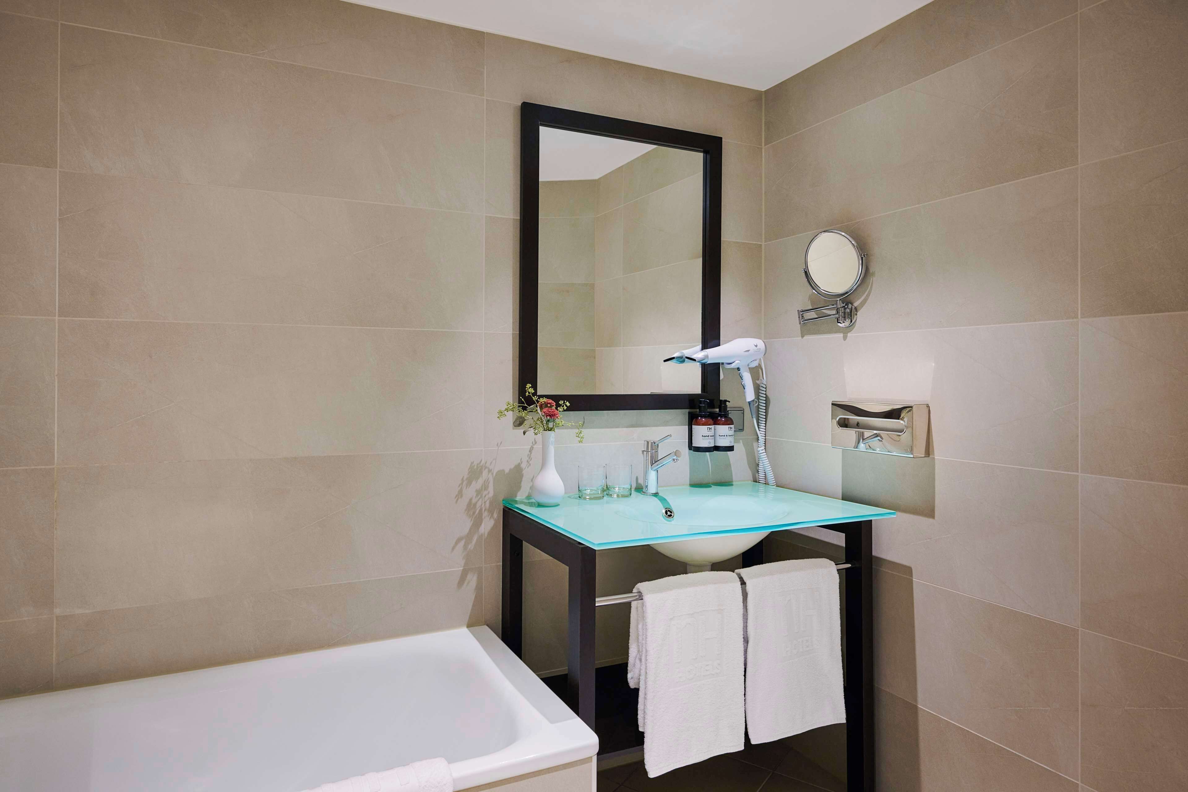 A bathroom with a glass sink, a white bathtub, and a large mirror.