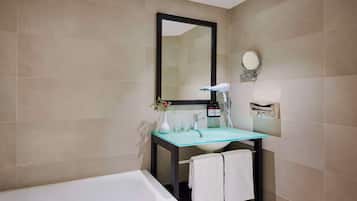 A bathroom with a glass sink, a white bathtub, and a large mirror.