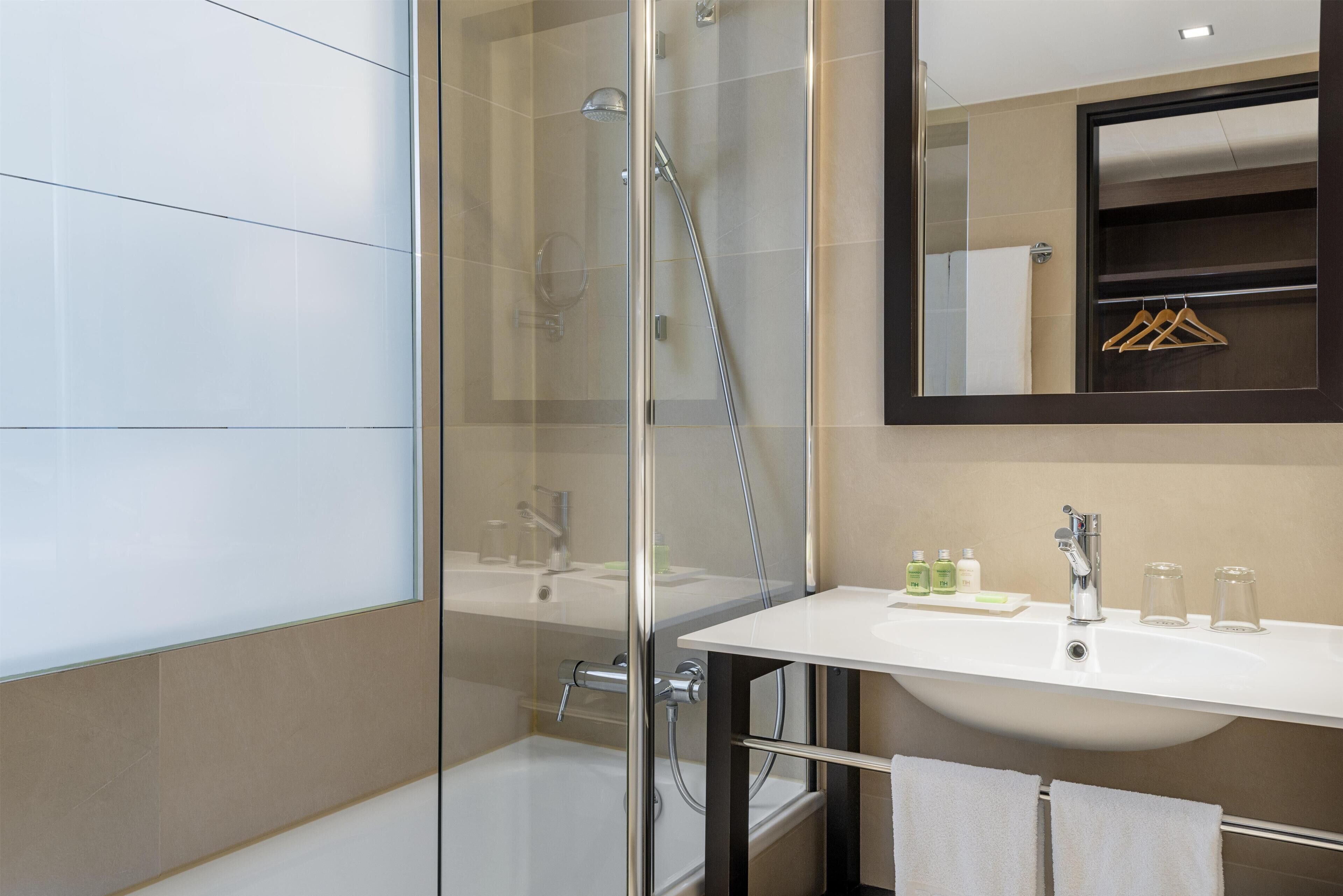 Un baño moderno con ducha de vidrio, lavamanos blanco y espejo con perchero de madera.