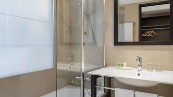 Un baño moderno con ducha de vidrio, lavamanos blanco y espejo con perchero de madera.