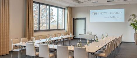 A conference room with a long table, chairs, and a projector screen displaying "nh HOTEL GROUP PART OF MINOR HOTELS".