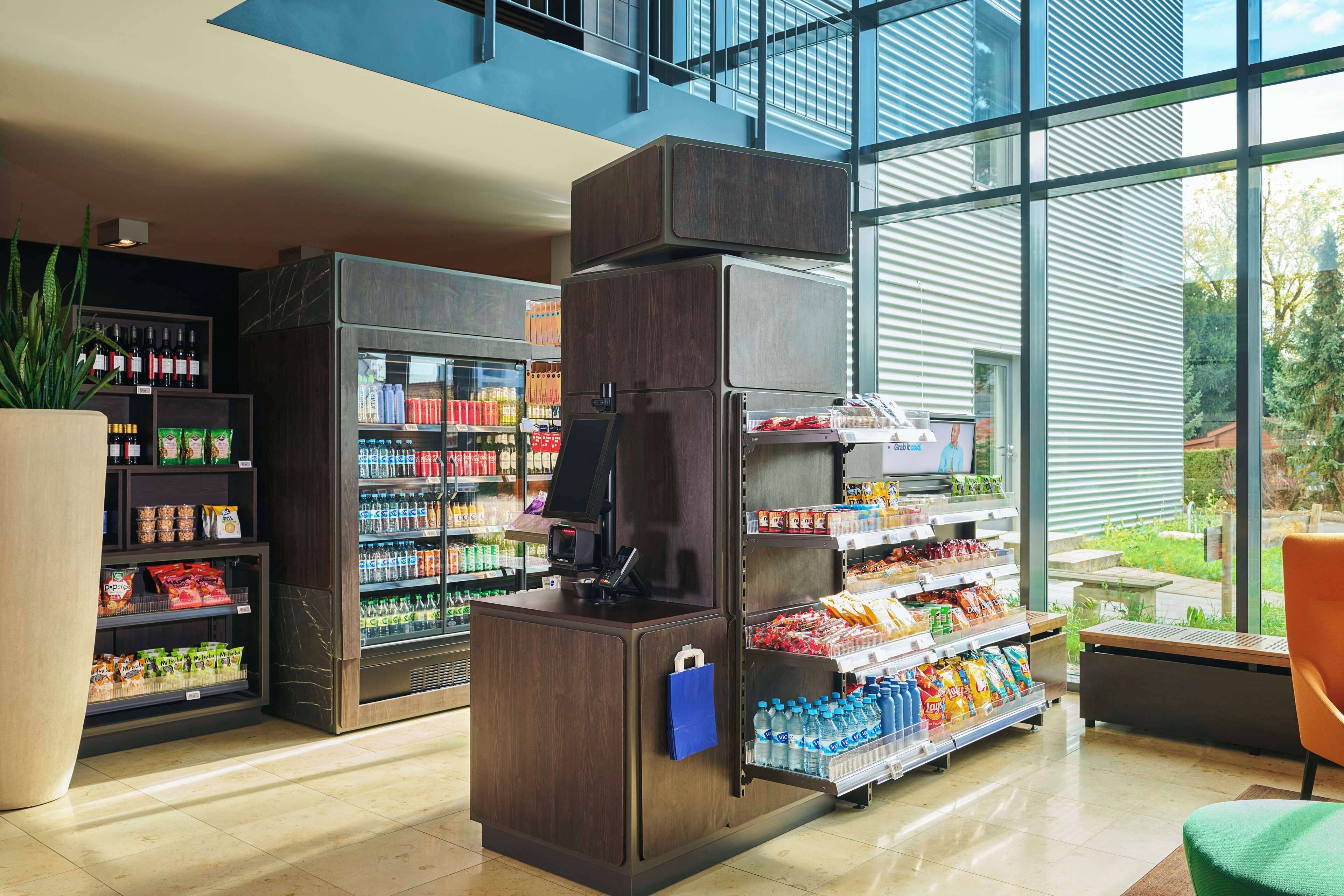 A modern grocery store with refrigerated sections, shelves stocked with beverages and snacks, and a seating area with a view of the outdoors.