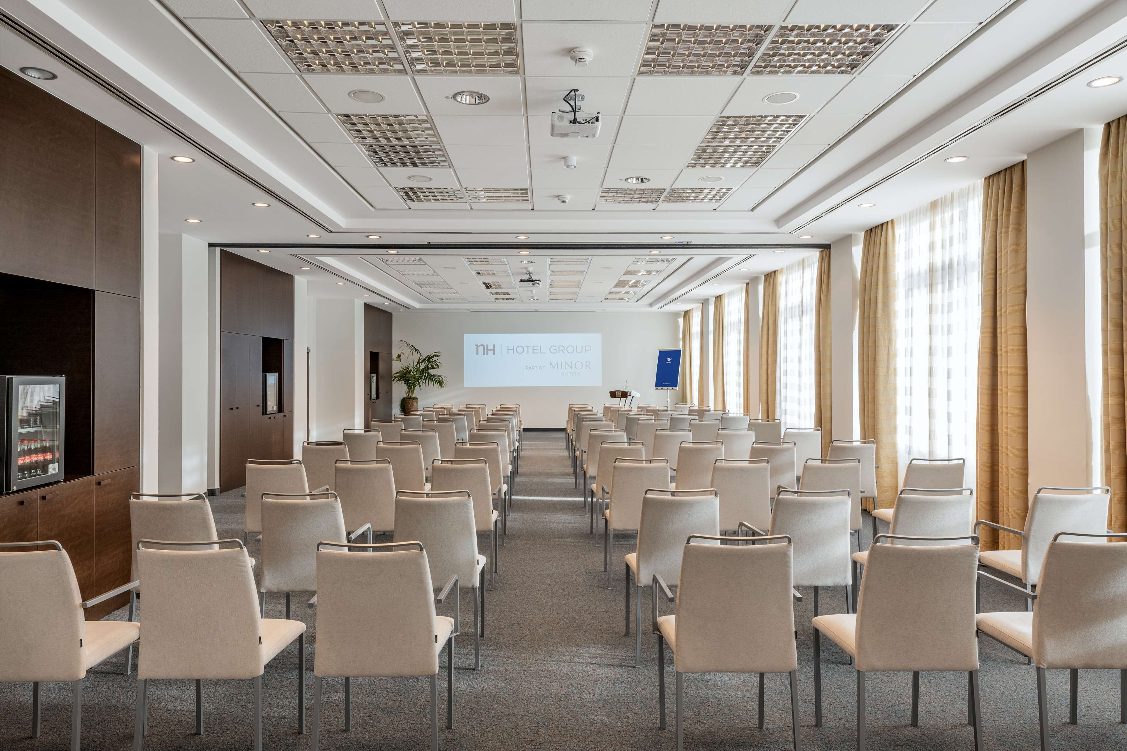 A hotel conference room with rows of chairs, a projection screen, and a presentation area.