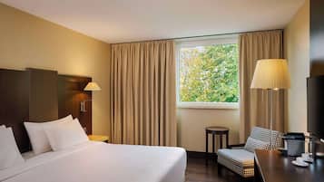 Une chambre d’hôtel avec un grand lit, un bureau, une chaise, une télévision et une fenêtre avec des rideaux.