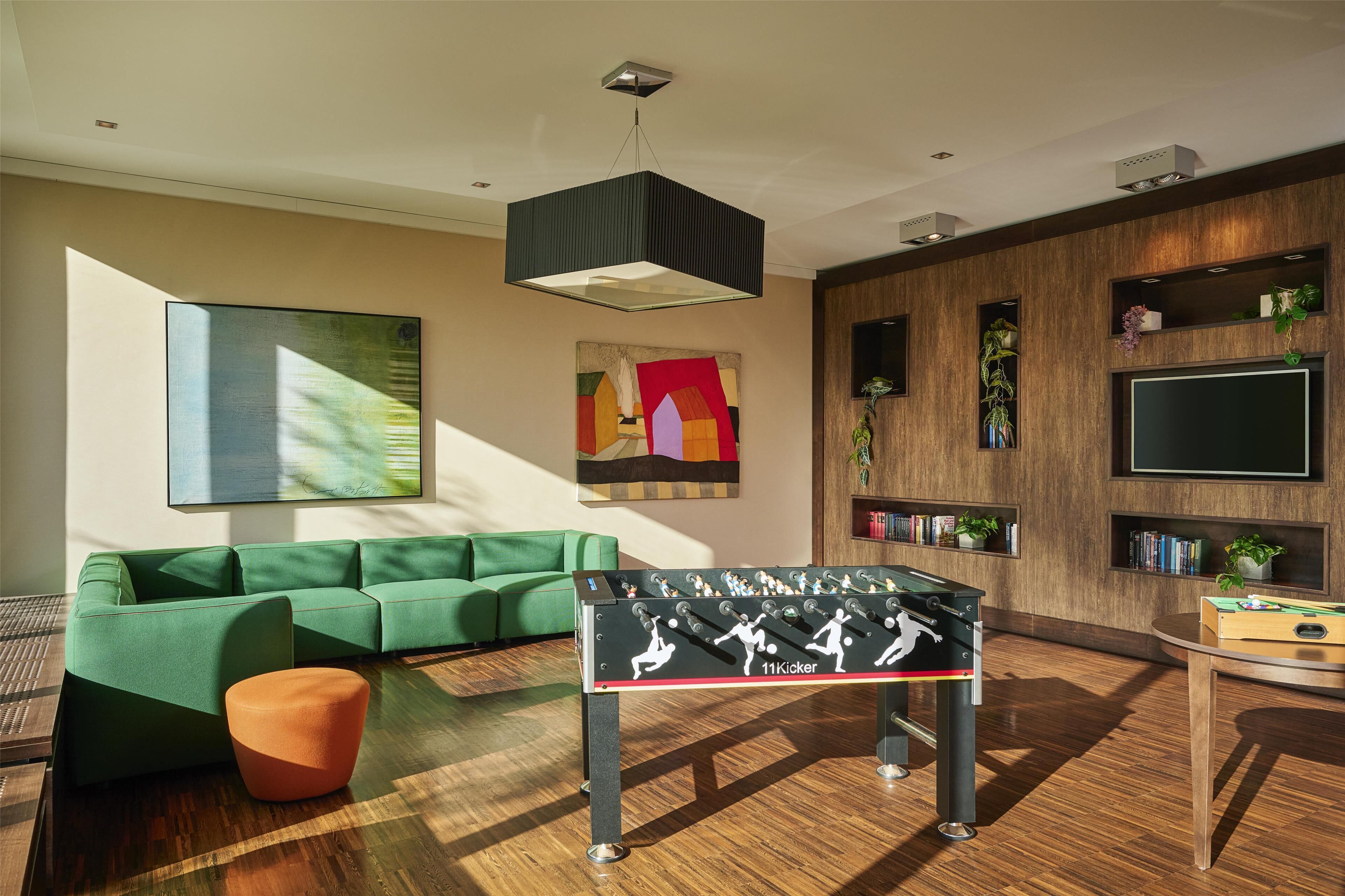 A modern living room with a green sofa, a foosball table, and a flat-screen TV mounted on the wall.