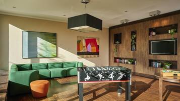 A modern living room with a green sofa, a foosball table, and a flat-screen TV mounted on the wall.