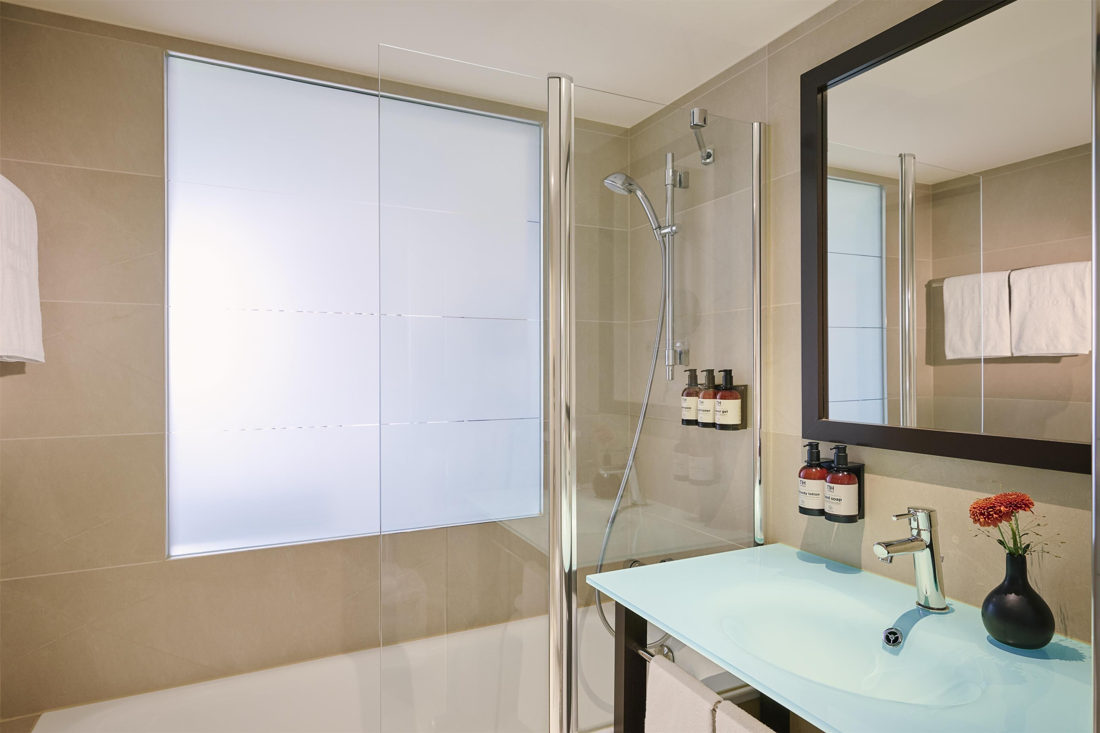 A modern bathroom with a glass shower enclosure, a vanity with a mirror, and toiletries on the wall.