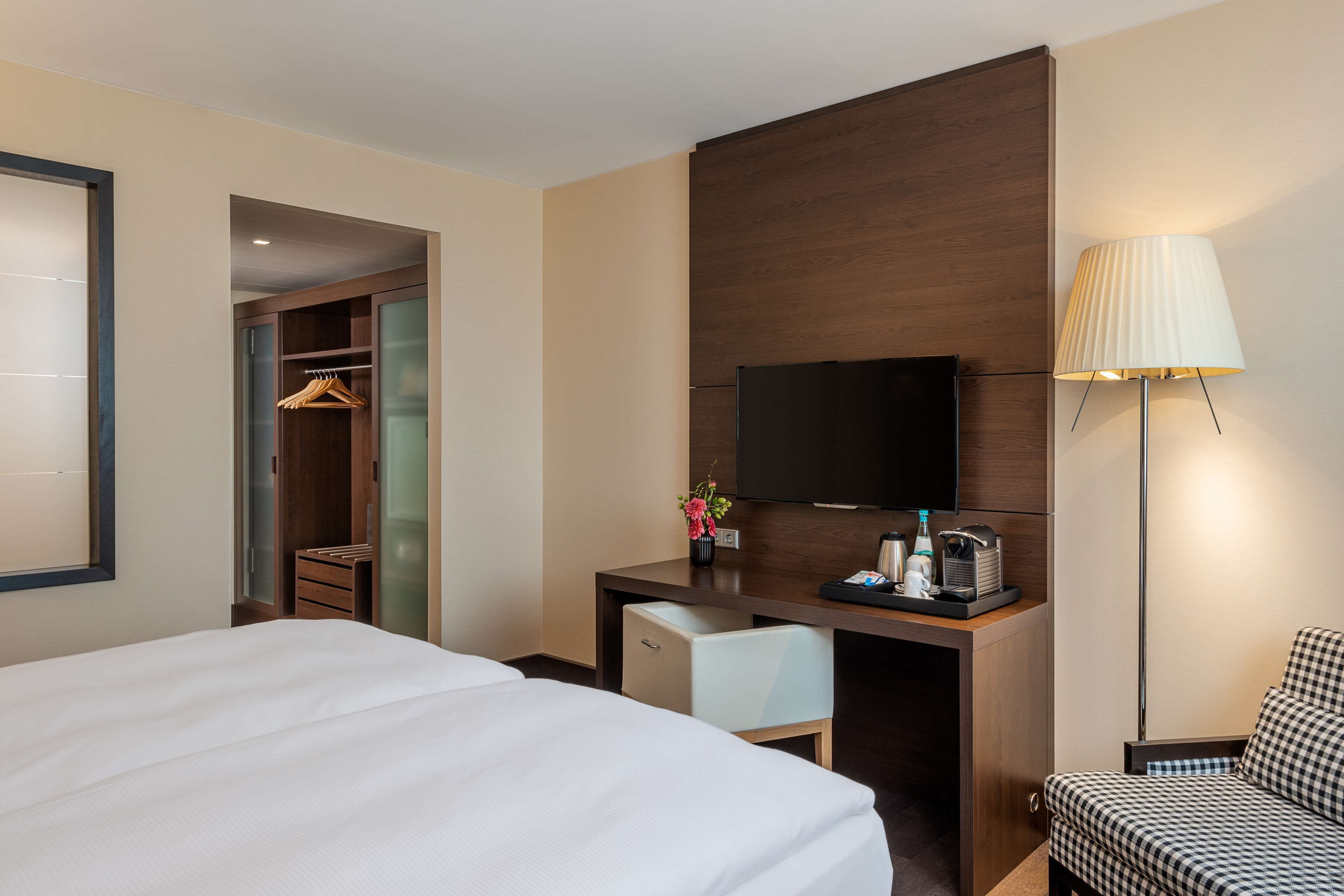 Habitación de hotel con cama, escritorio, televisor de pantalla plana, silla, armario y lámpara.