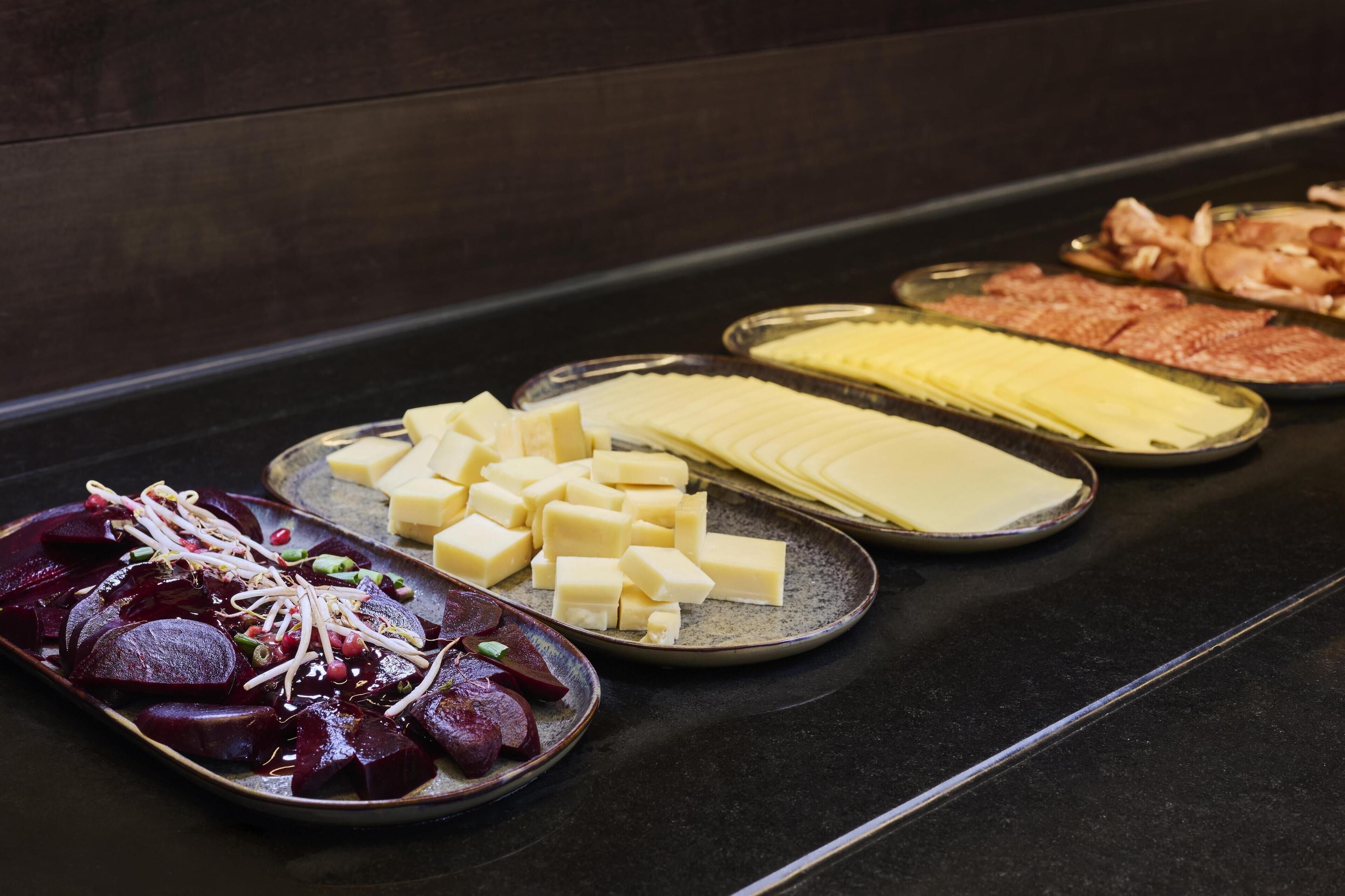 A buffet with various food items including cheese, meats, and vegetables.