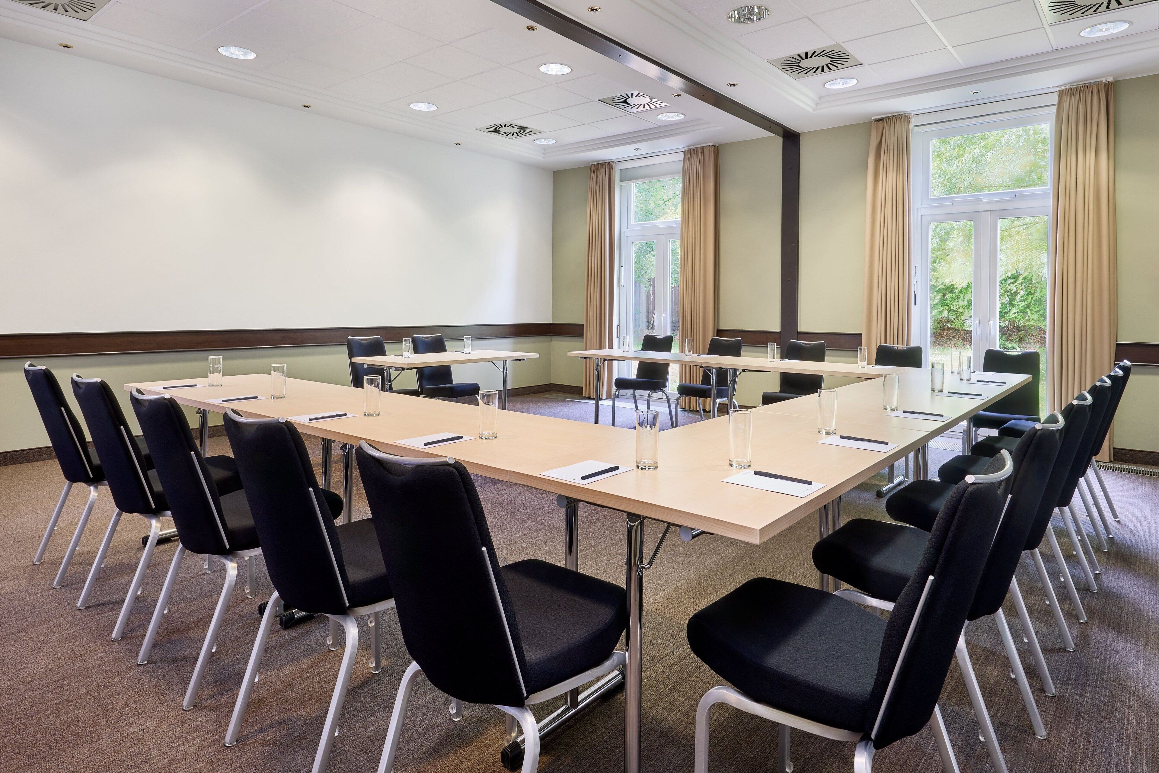 Une salle de conférence dotée d’une longue table, de chaises noires et de grandes fenêtres équipées de rideaux.