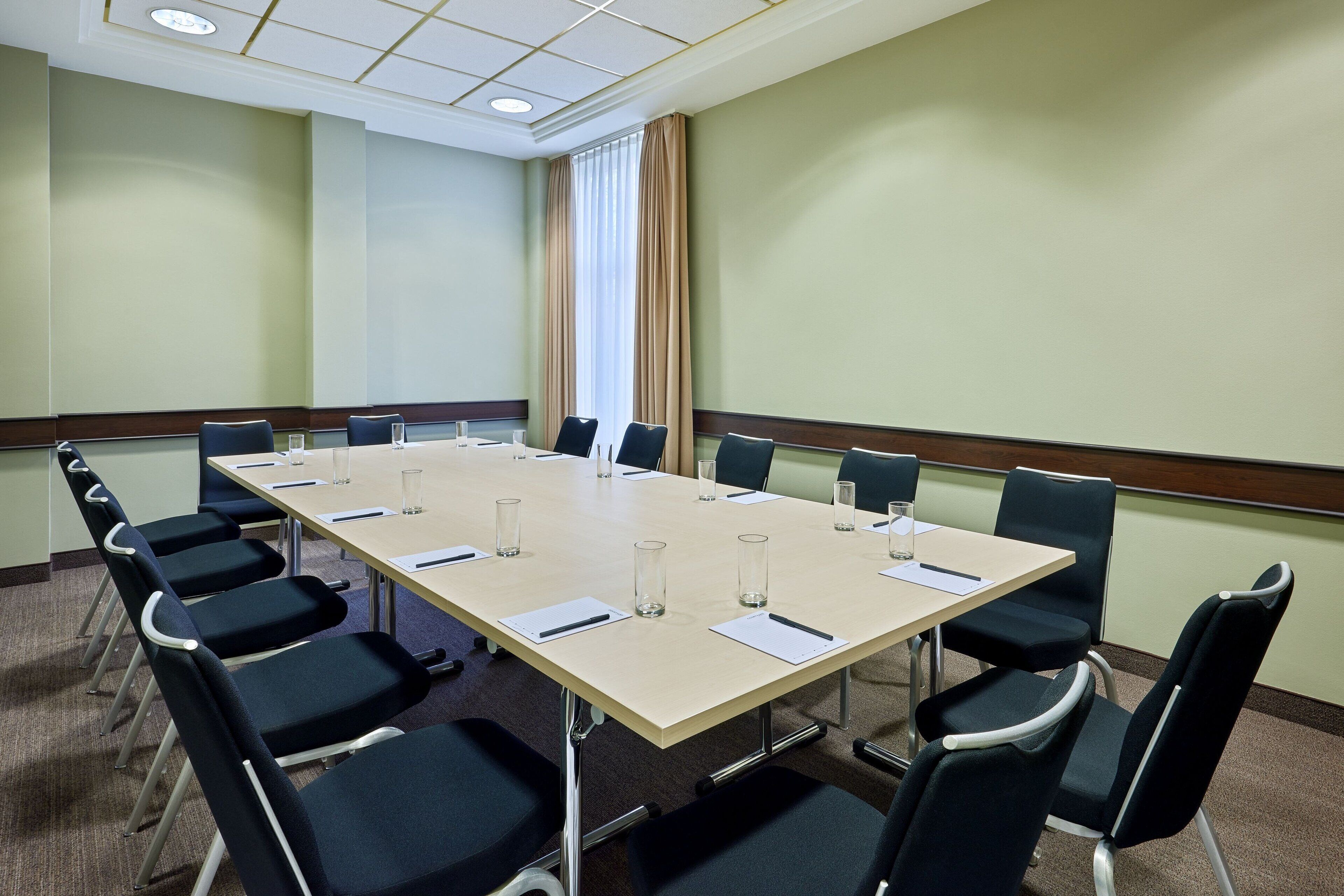 A conference room with a long table, chairs, and a window with curtains.