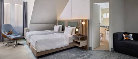 Una habitación de hotel moderna con dos camas, un área de estar y vistas al baño.