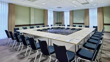 Uma sala de conferências com uma mesa comprida, cadeiras e piso coberto por carpete.