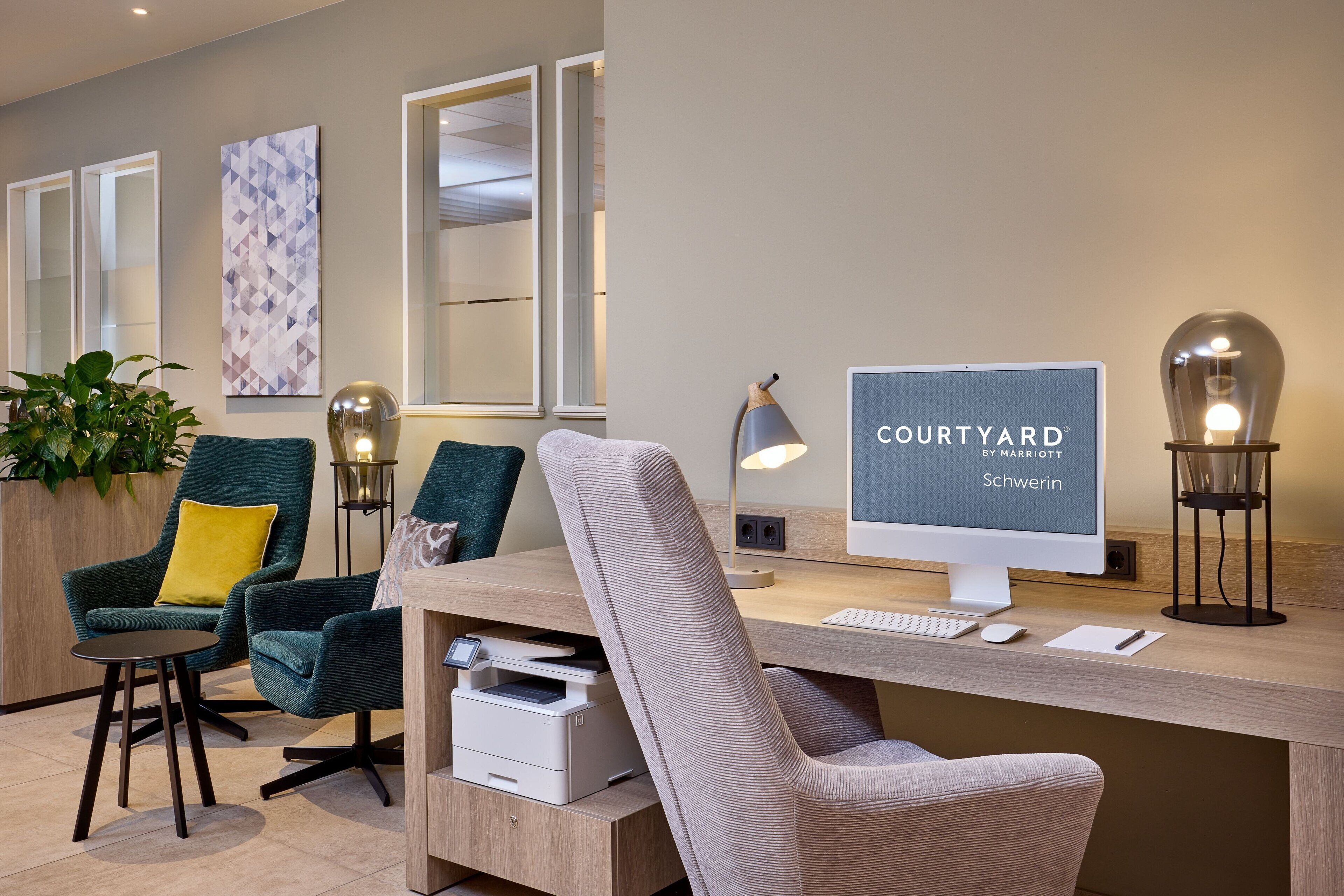 A modern hotel room with a desk, computer, and seating area.