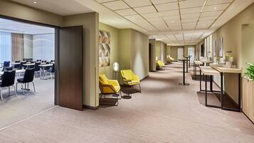 A hotel lobby with a long corridor, yellow chairs, a reception desk, and a large window with curtains.