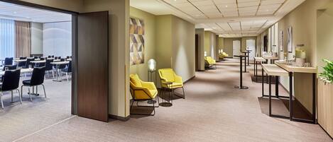 A hotel lobby with a long corridor, yellow chairs, a reception desk, and a large window with curtains.