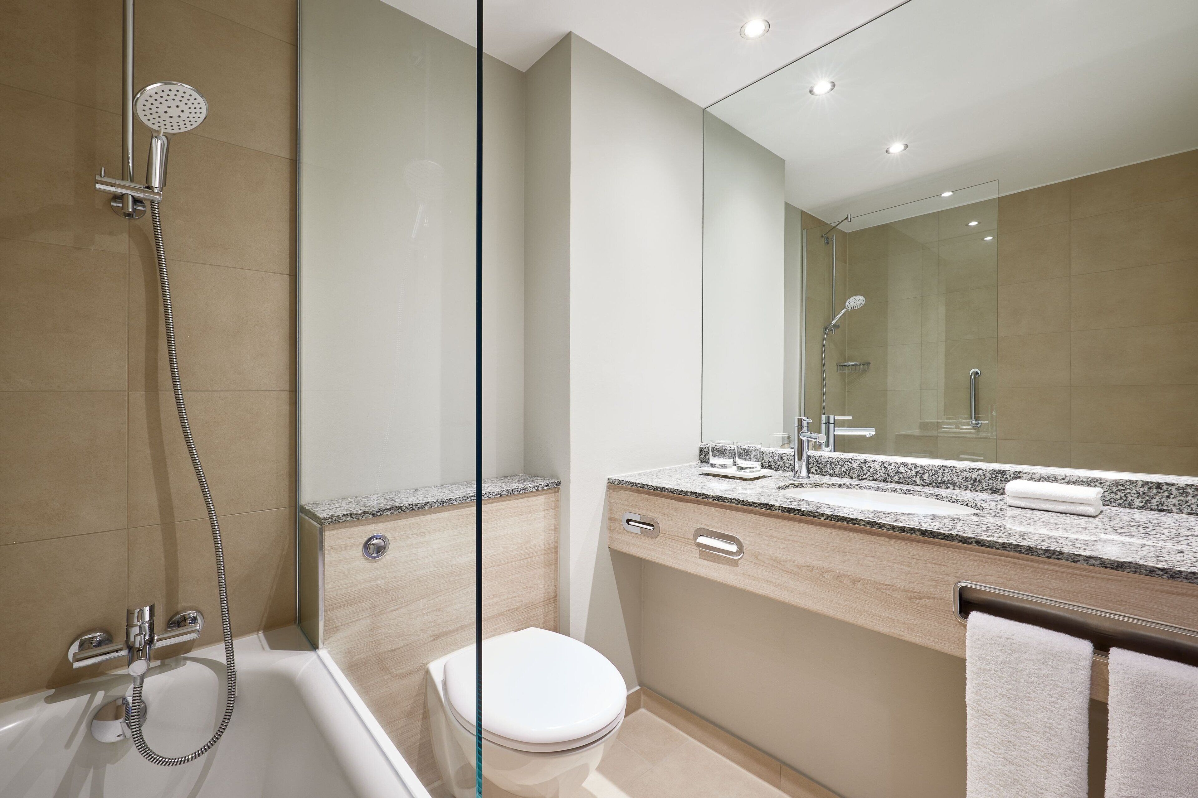 A modern bathroom with a glass shower enclosure, a bathtub, a toilet, and a vanity with a mirror.