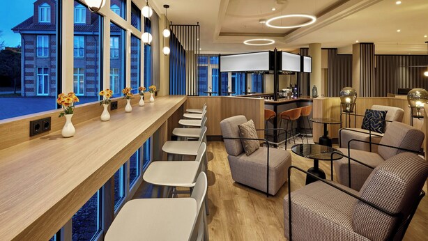 A modern hotel lobby with a long reception desk, seating area, and large windows offering a view of the building outside. - Courtyard by Marriott Schwerin (Schwerin)