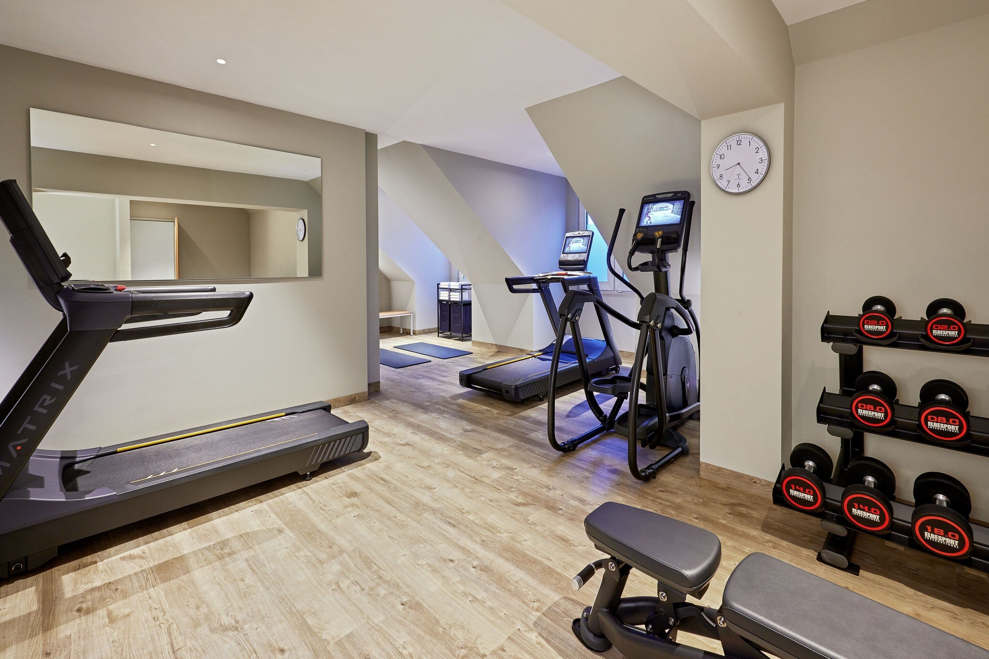Ein Heimfitnessraum mit Laufband, Crosstrainer, Bank und Hanteln.