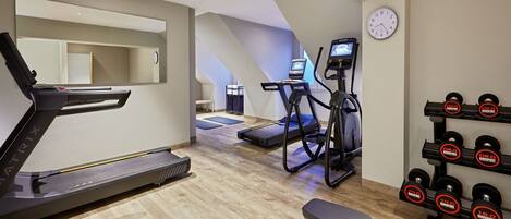A home gym with a treadmill, elliptical, bench, and dumbbells.