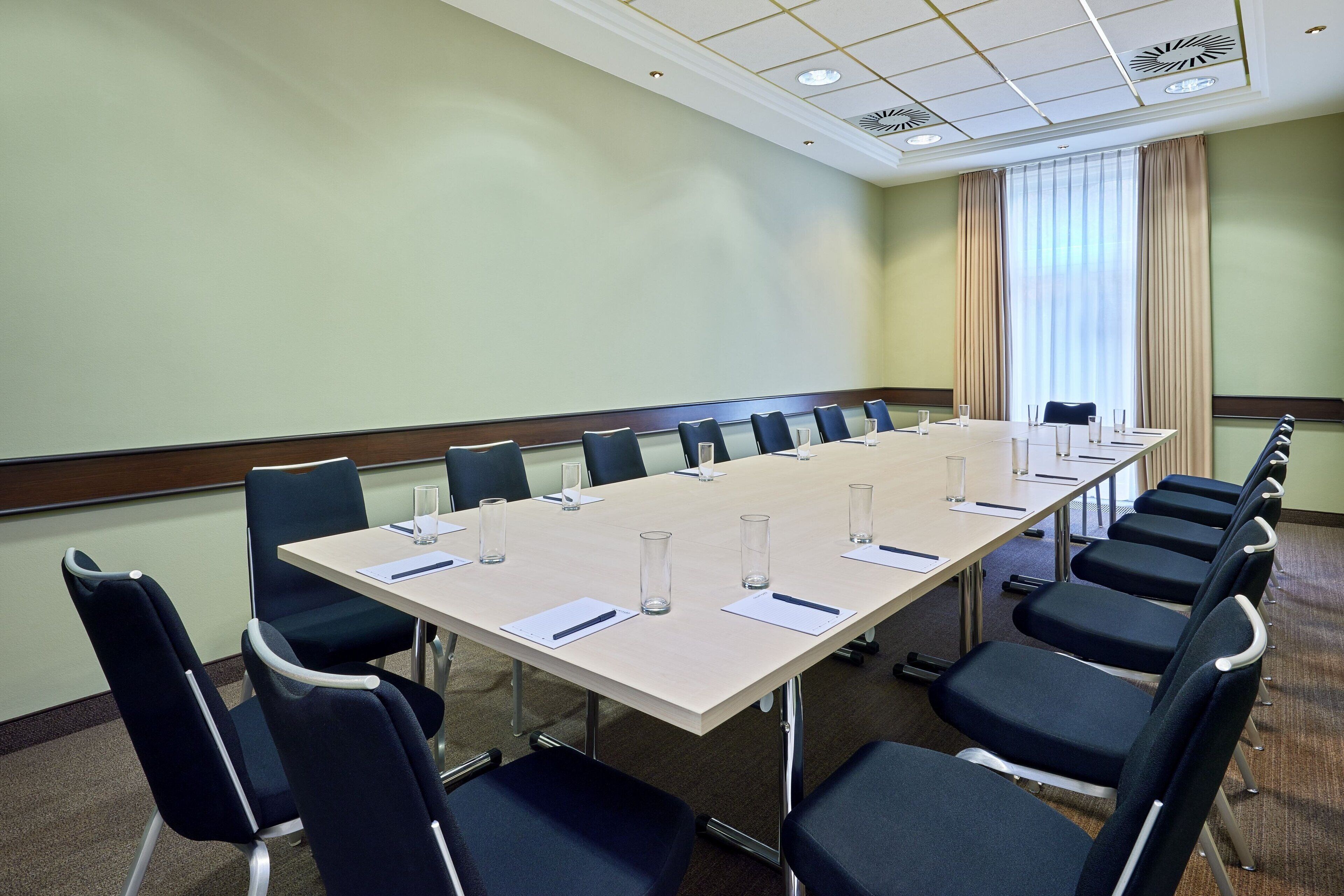Una sala de conferencias con una larga mesa, sillas y un ventanal con cortinas.