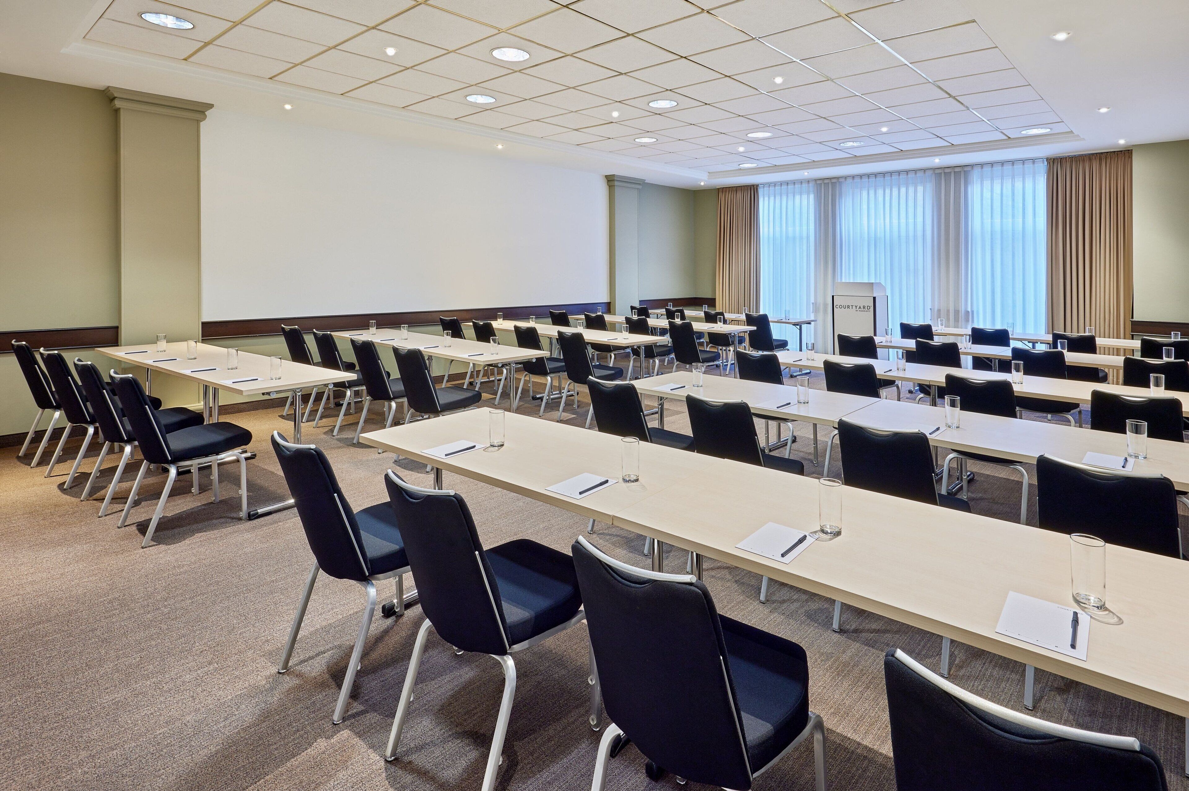 Un salón de conferencias con varias mesas y sillas, una pantalla de proyector y un atril.