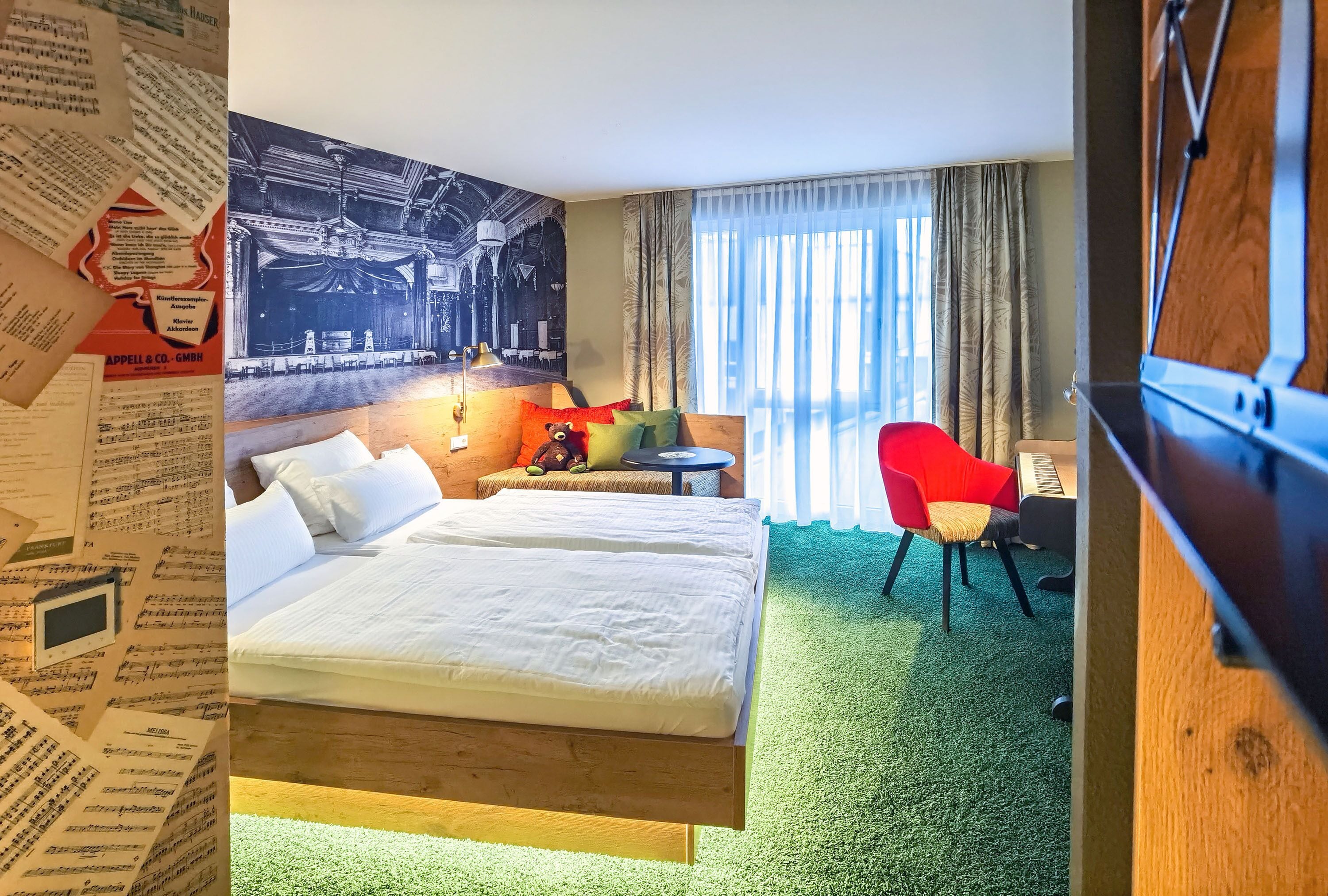 A hotel room with a large bed, a red chair, a small table, and a large window with curtains.