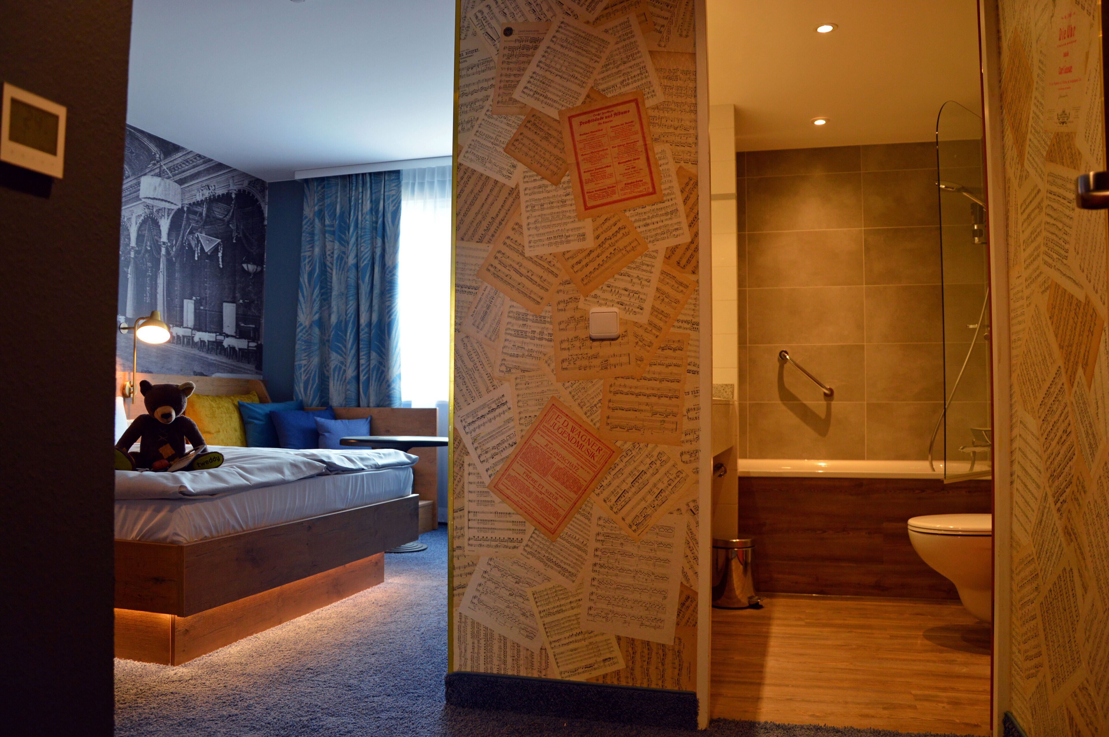 Une chambre à coucher avec un lit, un ours en peluche et un mur recouvert de papiers.