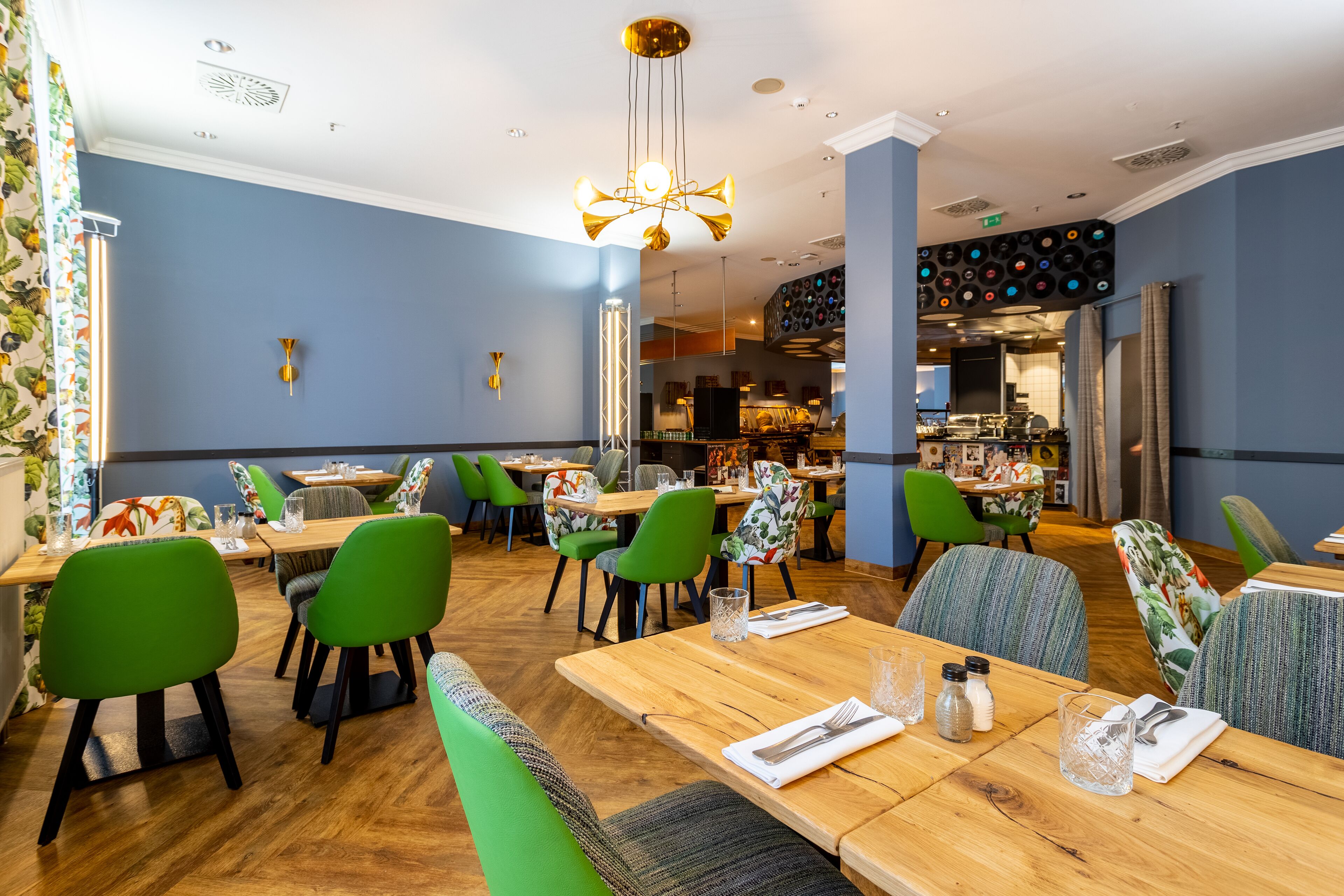 A restaurant with wooden tables and green chairs, a chandelier, and a wall with a record player.