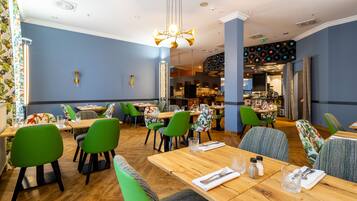 Un restaurant avec des tables en bois et des chaises vertes, un lustre et un mur orné d’un tourne-disque.