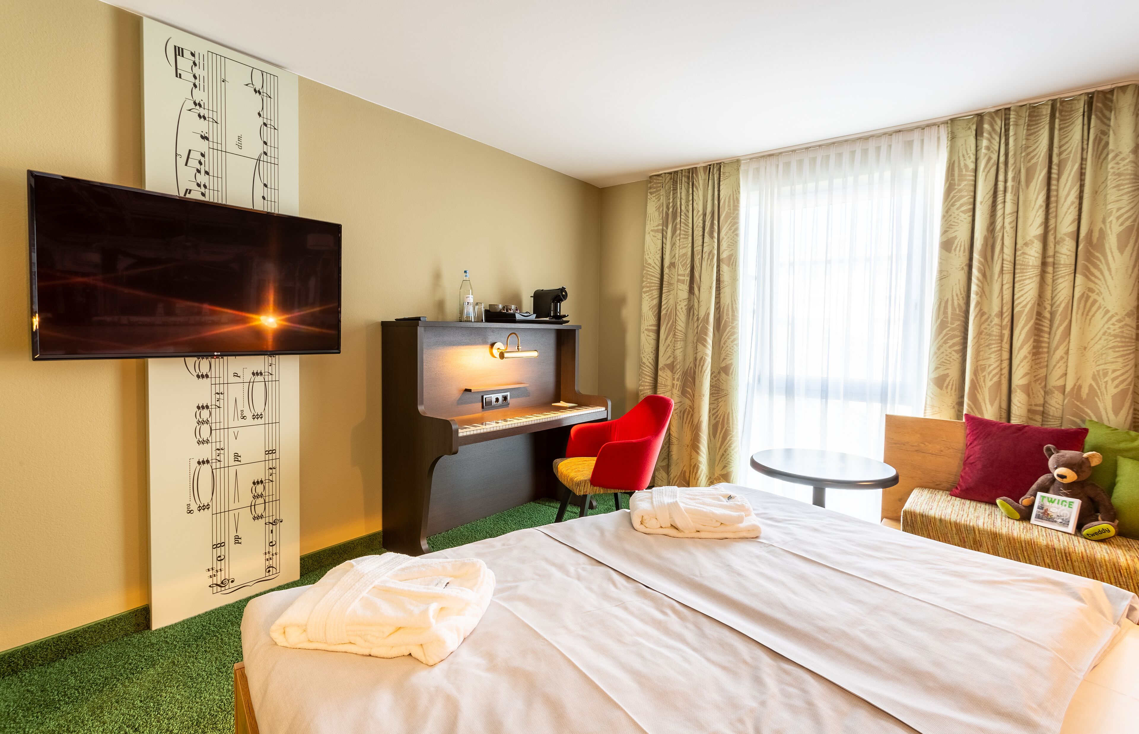 A hotel room with a bed, a desk with a computer, a TV, and a window with curtains.