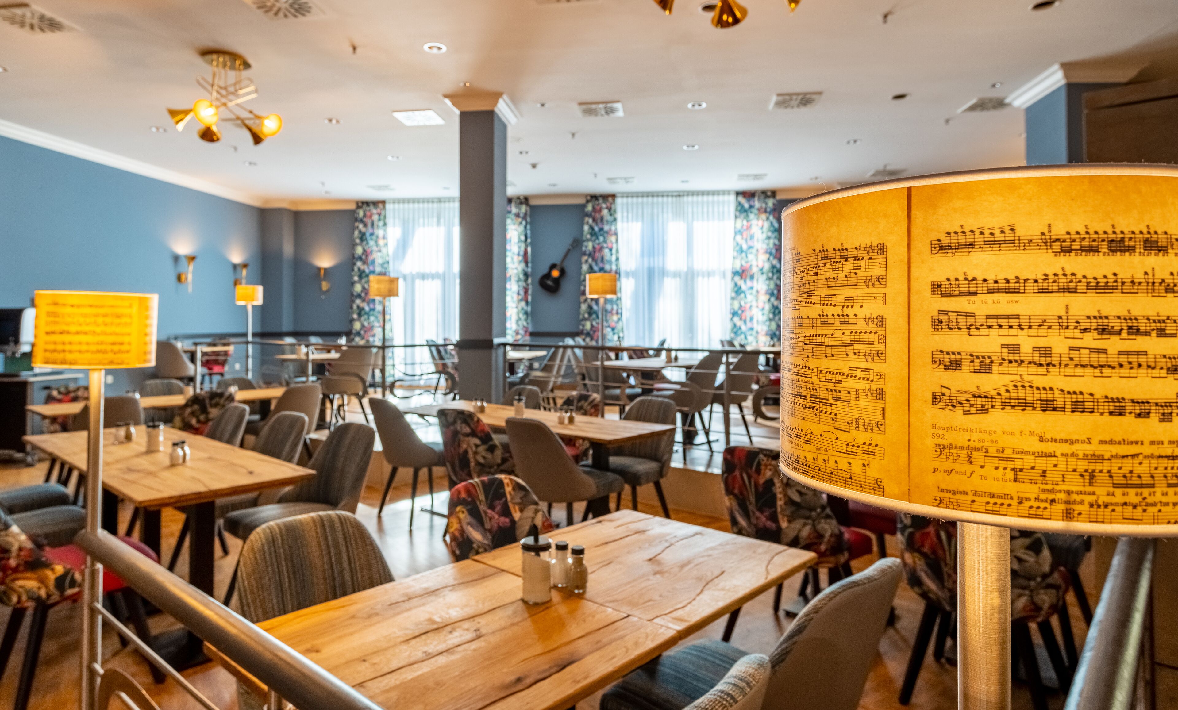 A spacious dining area with tables and chairs, a large window with curtains, and a wall with a musical score.