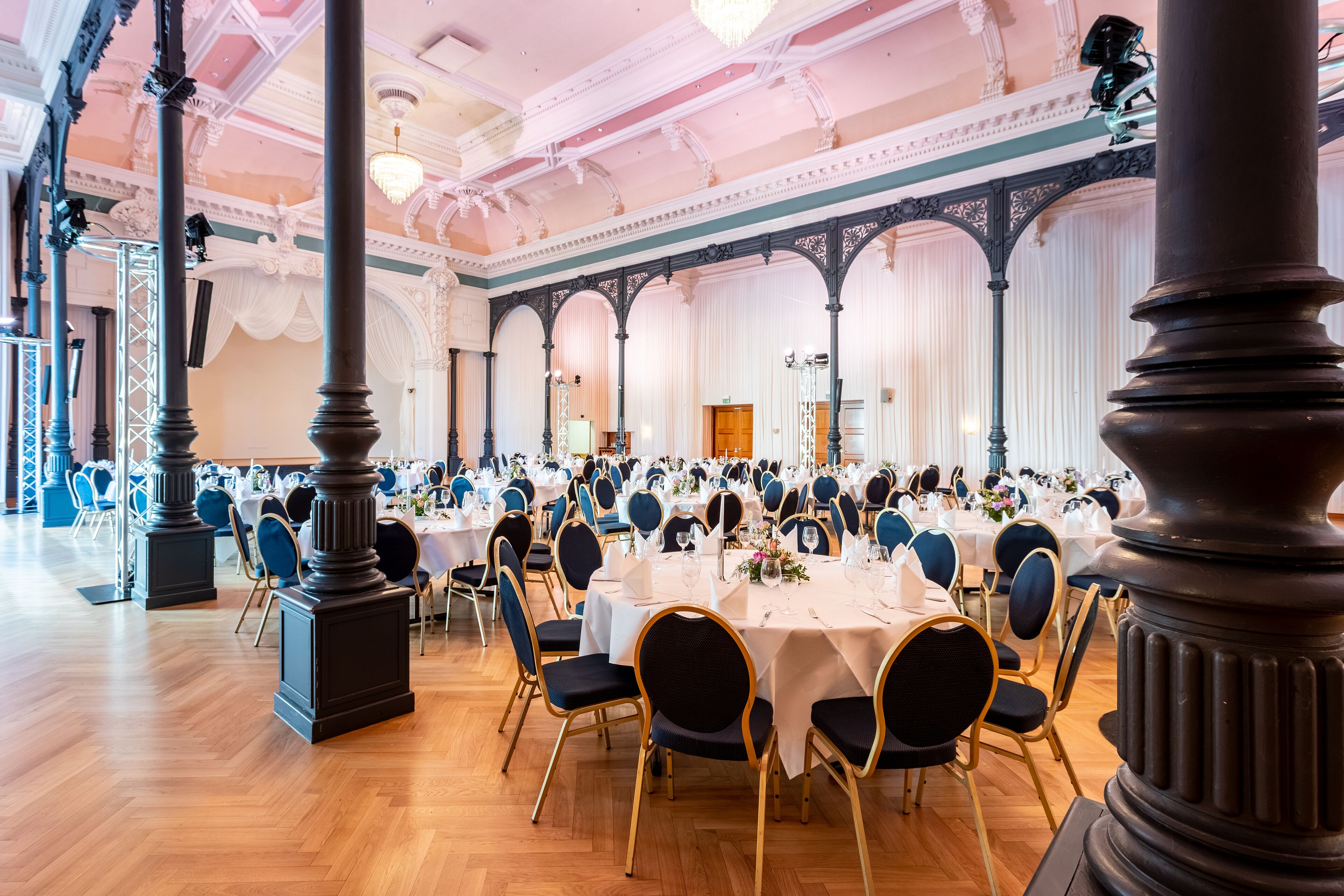 A banquet hall with round tables, blue chairs, and ornate columns.