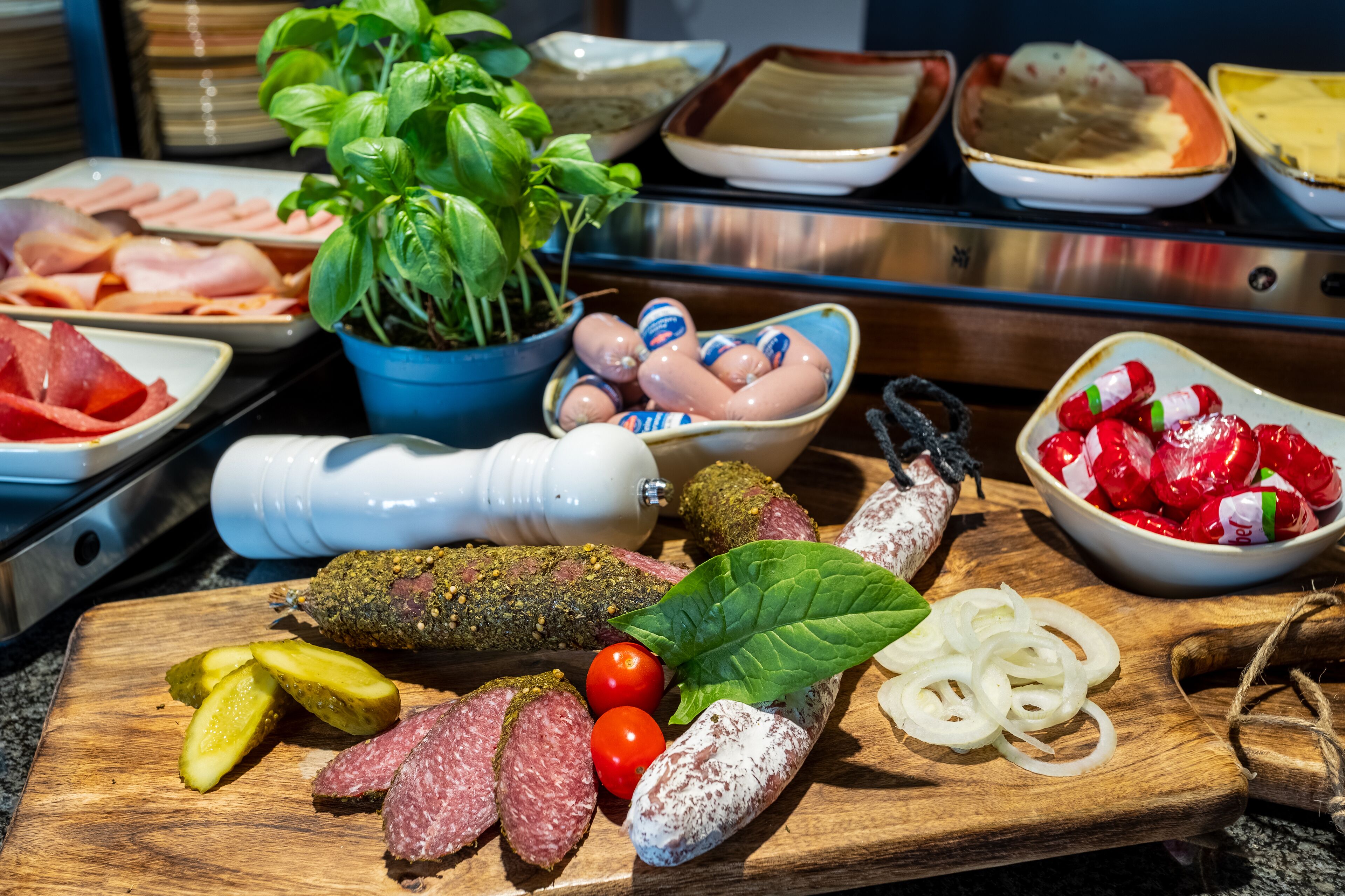 Una selección de embutidos curados, encurtidos y verduras frescas sobre una tabla de madera.