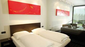 A hotel room with a bed, a sofa, and two red abstract paintings on the wall.