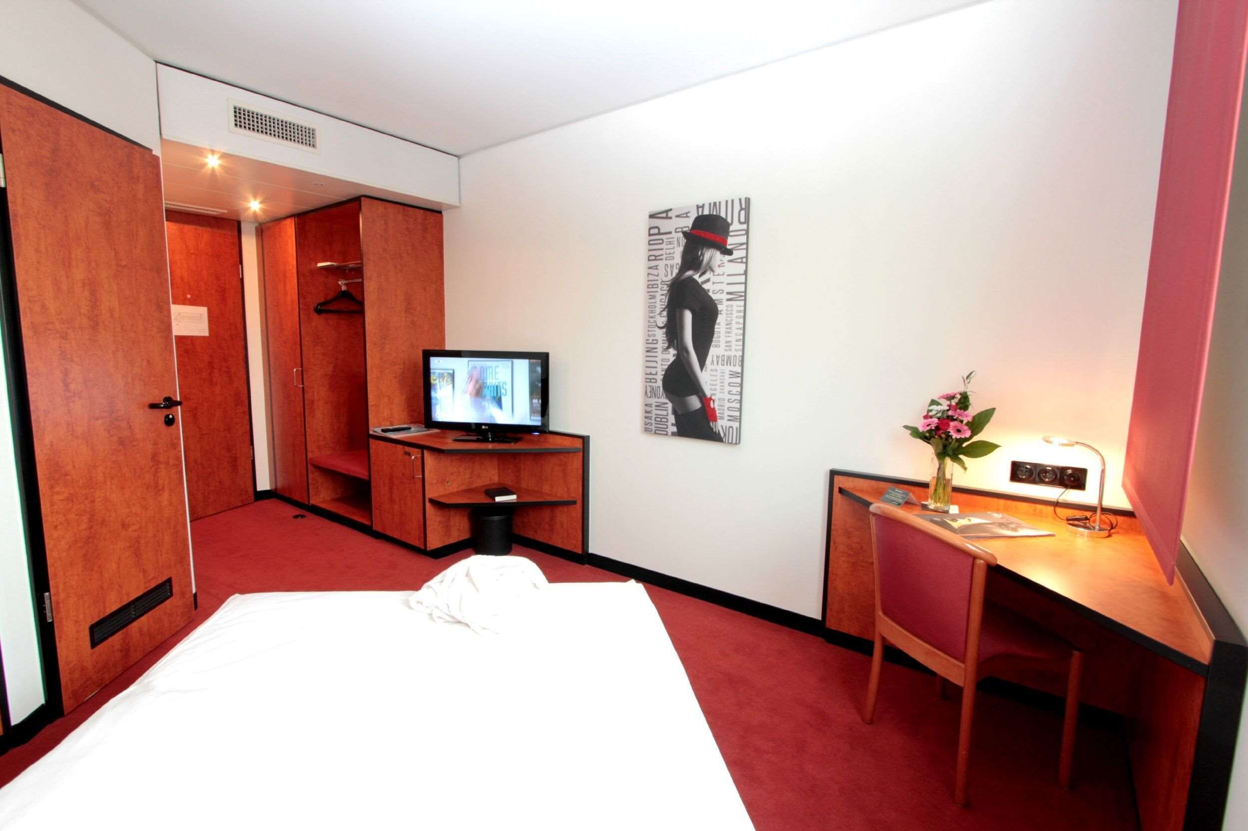 Quarto de hotel com uma cama, uma escrivaninha com computador, televisão e guarda-roupa.