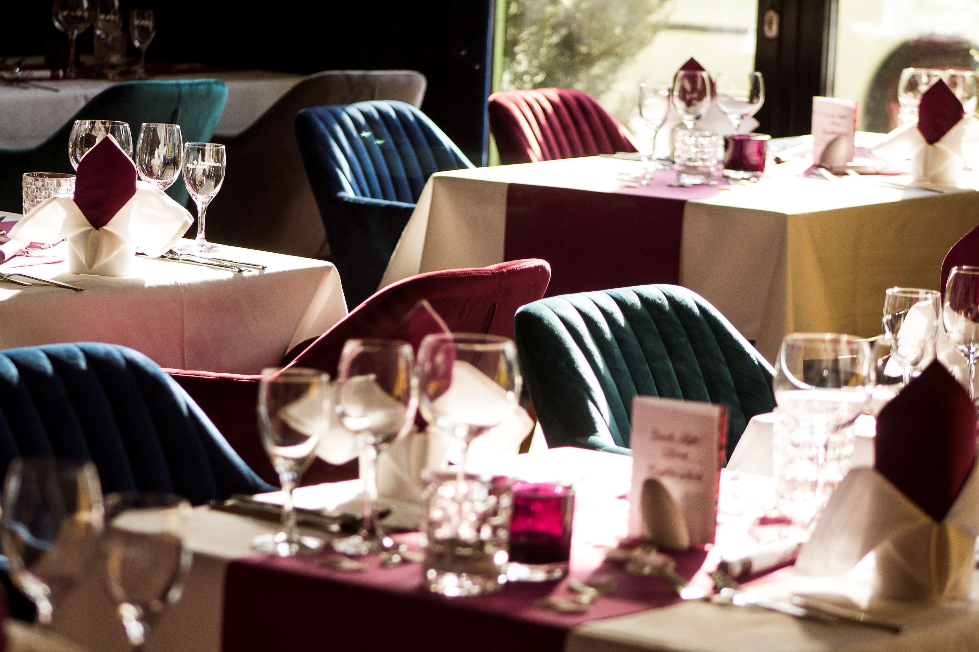 A restaurant setting with tables set for dining, chairs upholstered in different colors, and wine glasses on the tables.