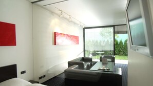 A modern hotel room with a bed, a seating area with a table, and a large window offering a view of greenery outside. - ARA-Hotel Comfort (Ingolstadt)