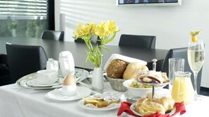 A breakfast setting with a table set for two, including plates, bread, pastries, a jug of juice, and a glass of white wine. - ARA-Hotel Comfort (Ingolstadt)
