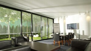 A modern hotel room with a large window, a dining area with a table and chairs, and a flat-screen TV mounted on the wall. - ARA-Hotel Comfort (Ingolstadt)