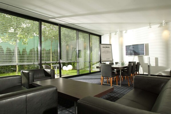 A modern hotel room with a large window, a dining area with a table and chairs, and a flat-screen TV mounted on the wall.