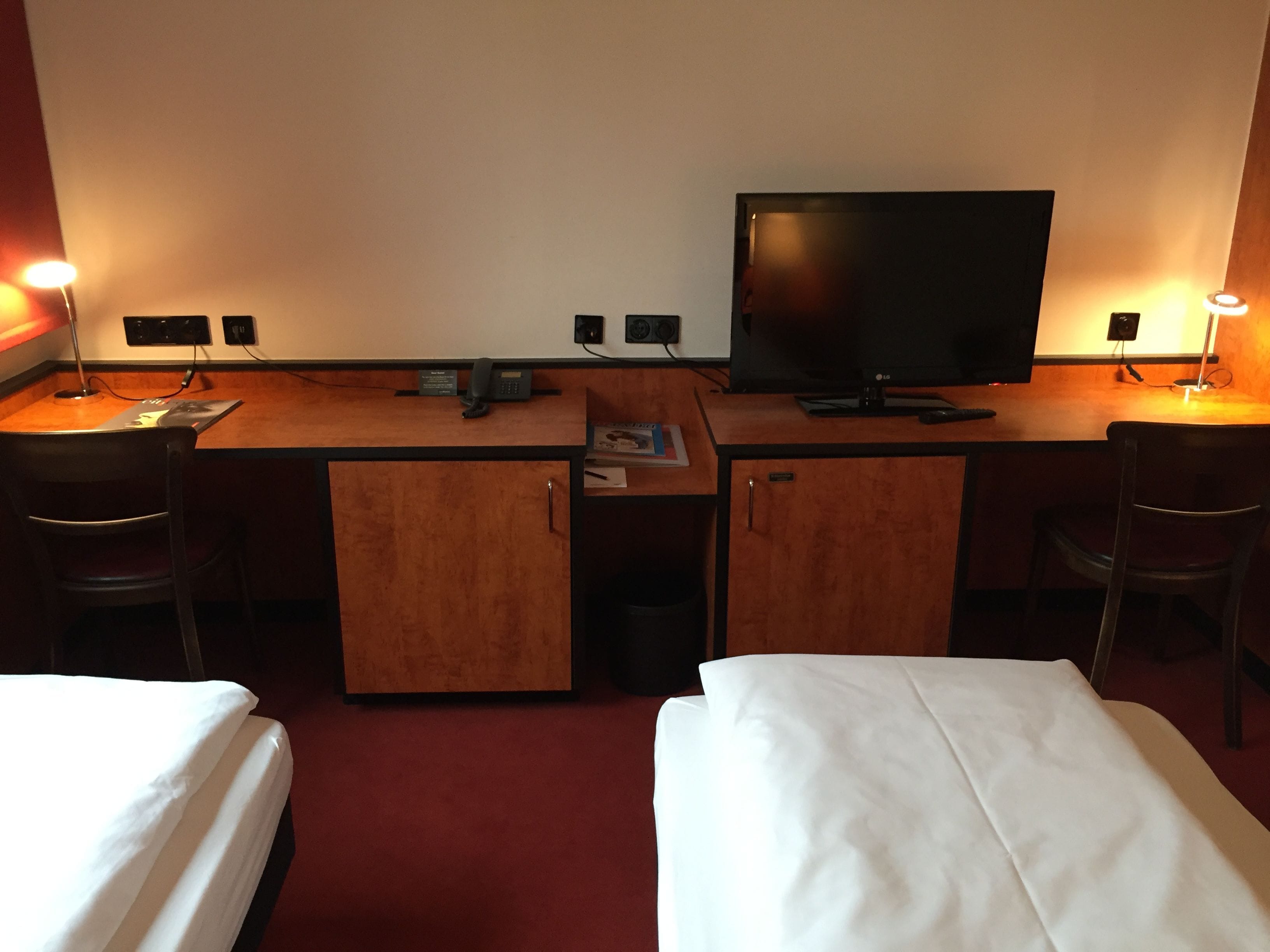 Una habitación de hotel con dos camas individuales, un escritorio con computadora y teléfono, una televisión y dos sillas.