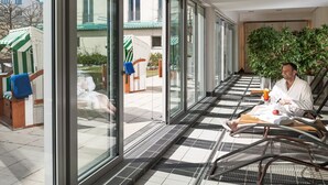A sunlit indoor area with large windows, a checkered floor, and a person relaxing on a chair with a drink. - Dorint Hotel Potsdam (Potsdam)